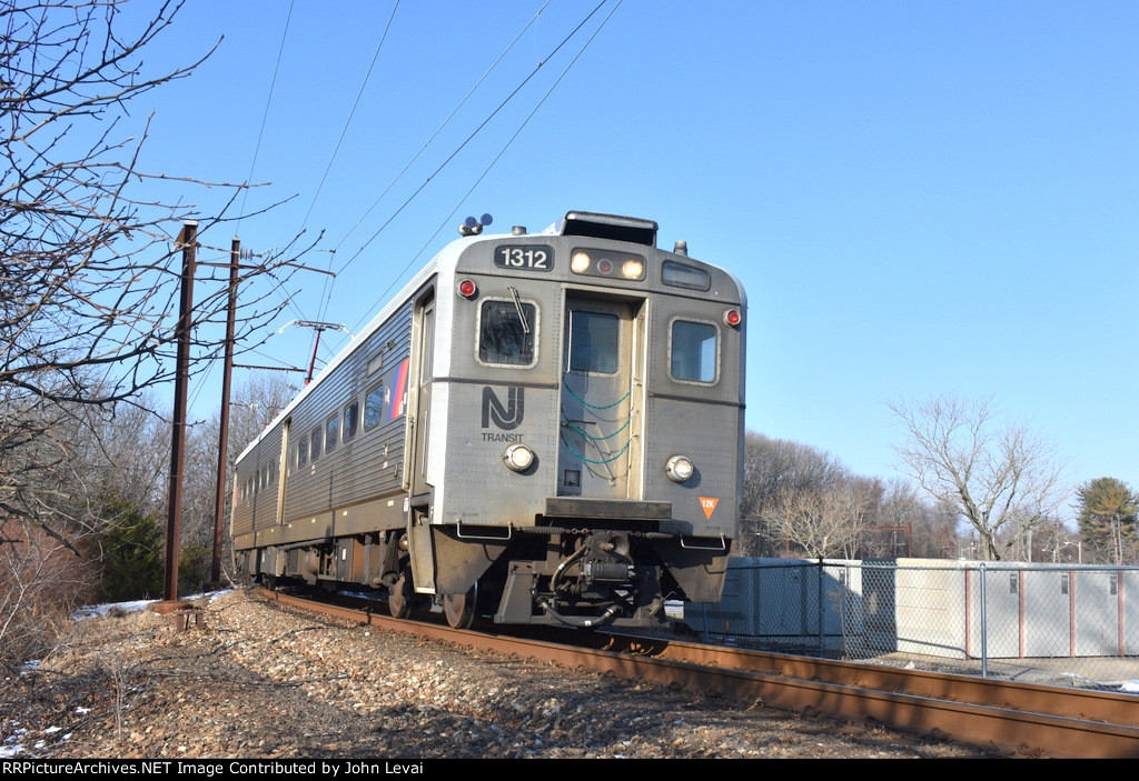 The eastbound NJT Princeton Dinky rounding the bend on the right of way bisecting the parking lot on the westbound side of Princeton Jct Station